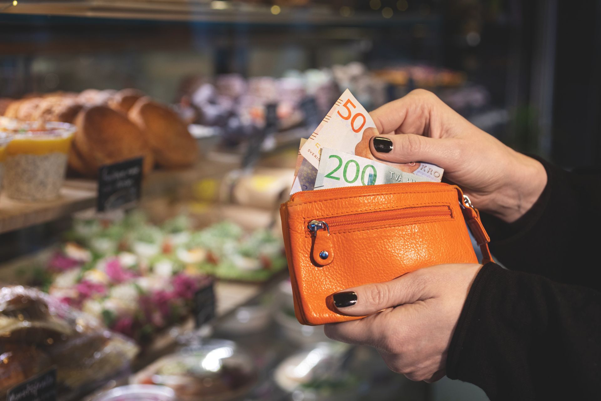 A close up of an orange wallet with cash notes being drawn out