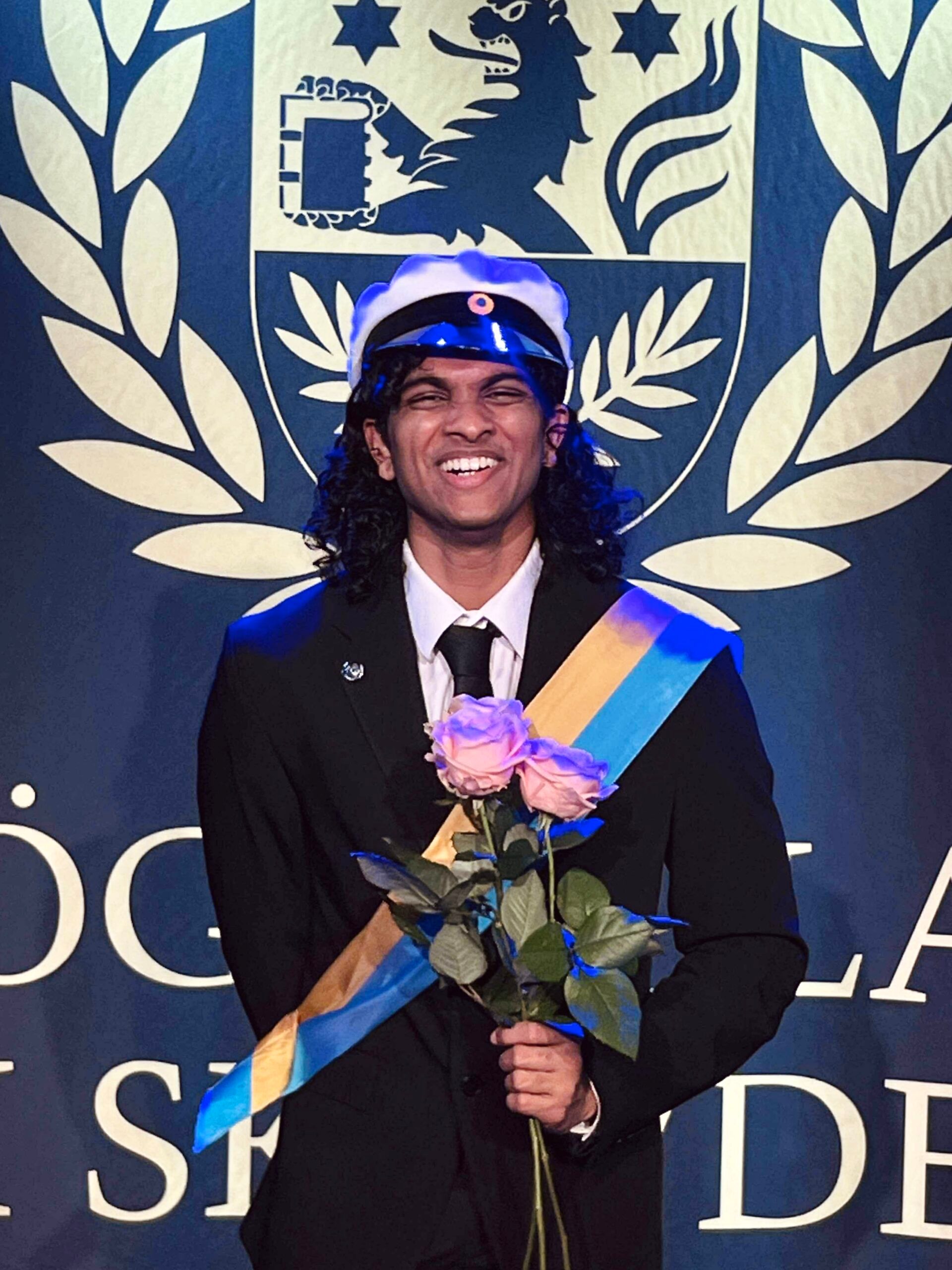 a student laughing at the camera with several pink roses in his hands