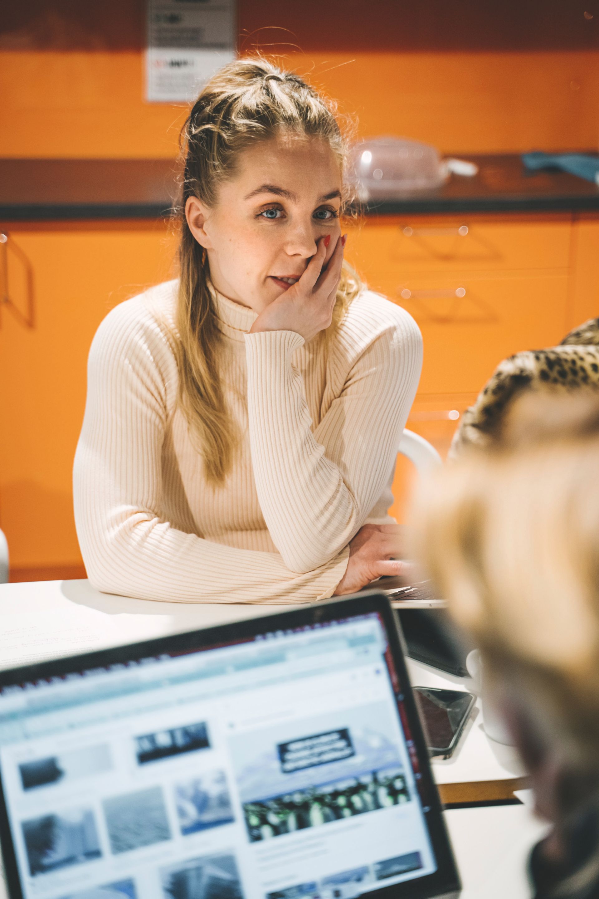 A young woman sits at a desk with others.