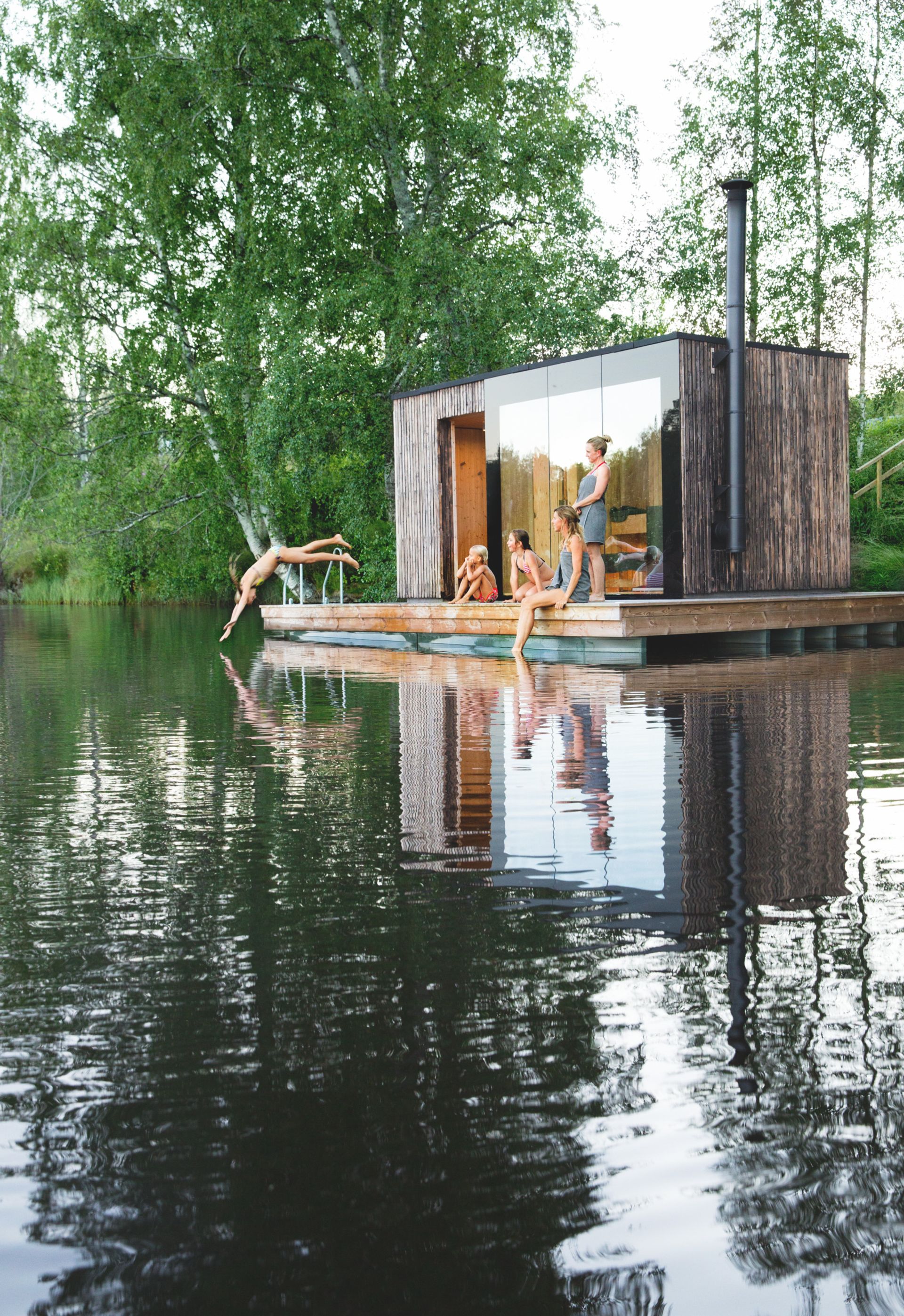 A group of people outside a sauna overlooking a lake